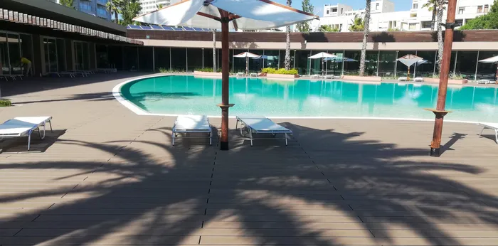 Parasol et bain de soleil près d'un massif de plantes, angle de la piscine de l'hôtel.