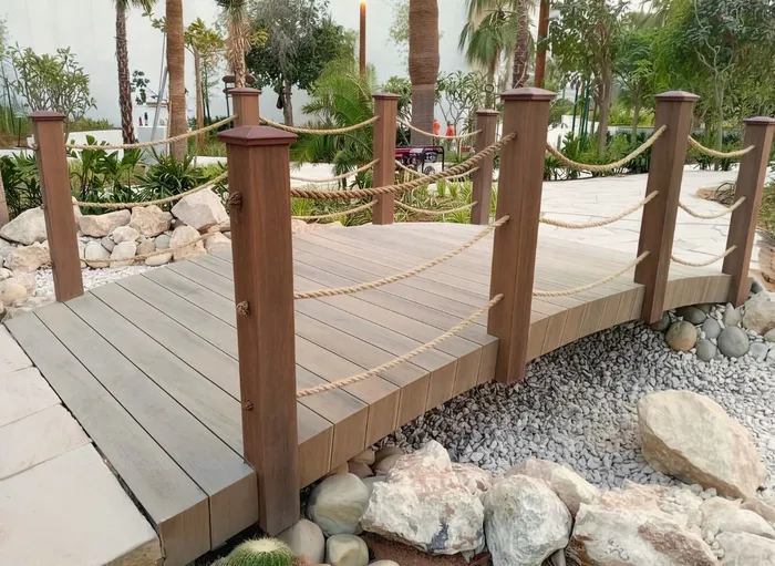 Passerelle courbe en terrasse composite avec garde-corps en corde, au milieu d'un jardin tropical.