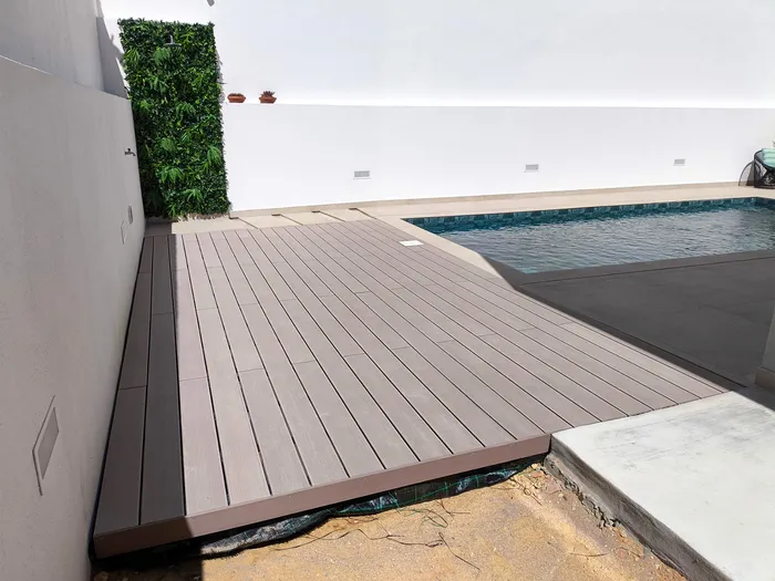 Vue en diagonale de la terrasse composite CDECK® Beige Rose fraîchement posée aux abords de la piscine, mur végétal en arrière-plan.