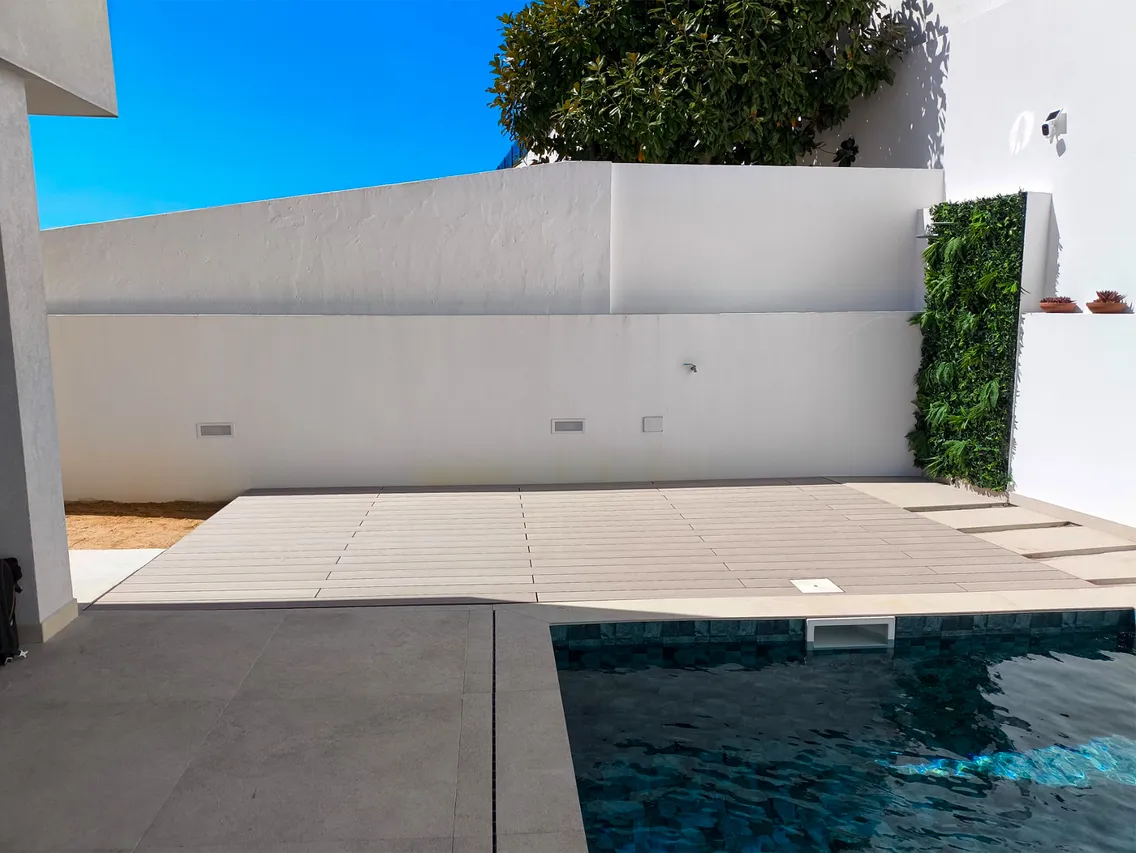 Vue d'ensemble de l'angle piscine avec la terrasse composite CDECK® Beige Rose, murs blancs et haie végétale, ciel bleu en arrière-plan.