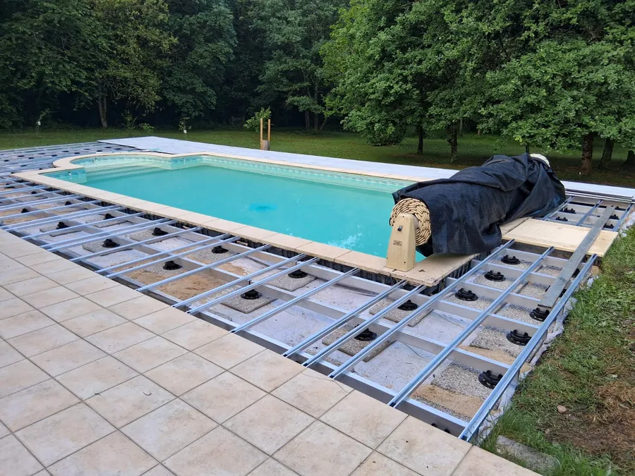 Ossature aluminium sur plots entourant la piscine, eau turquoise et terrasse pas encore posée.