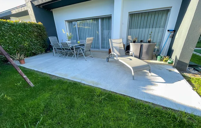 Petit patio en dalles de béton et carrelage disparates, avant travaux, salon de jardin contre la haie.
