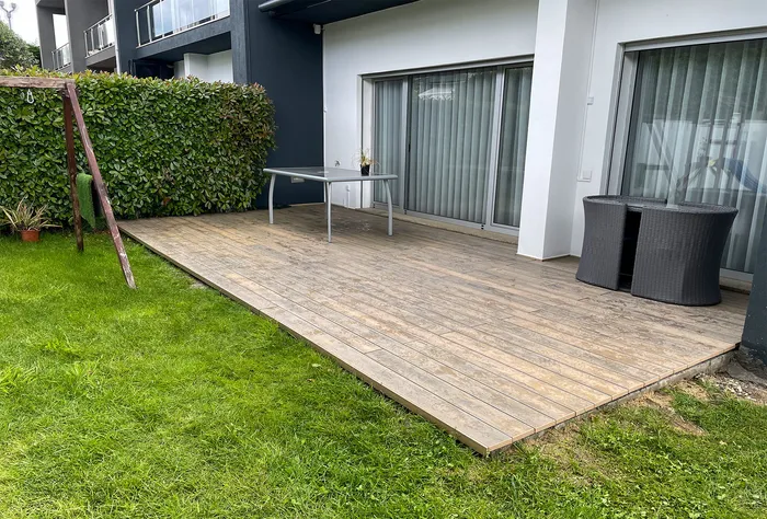 Terrasse composite Natural Beech agrandie jusqu'à la pelouse, balancelle et salon de jardin, immeuble voisin en arrière-plan.