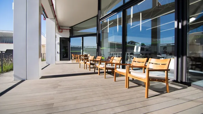 Grey composite decking balcony with wooden armchairs lined up beside the glazed office façade.