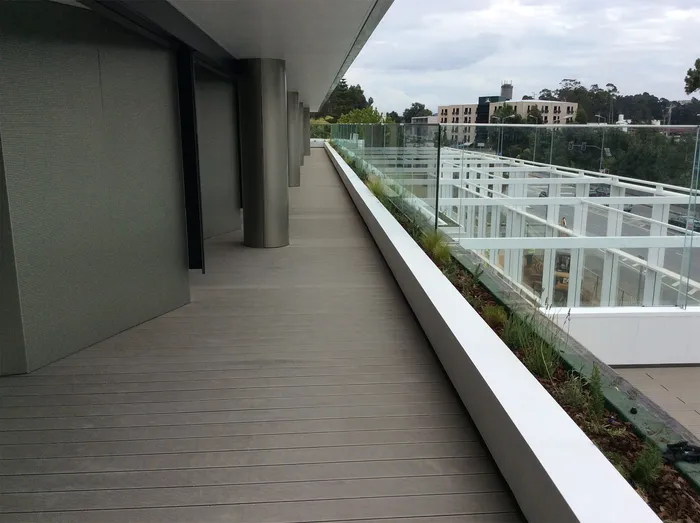 Grey composite decking balcony between the façade and the planter, overlooking the avenue and neighbouring buildings.
