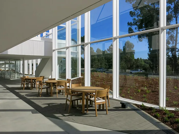 Covered terrace in grey composite decking with round wooden tables, beside the glazed ground-floor façade.