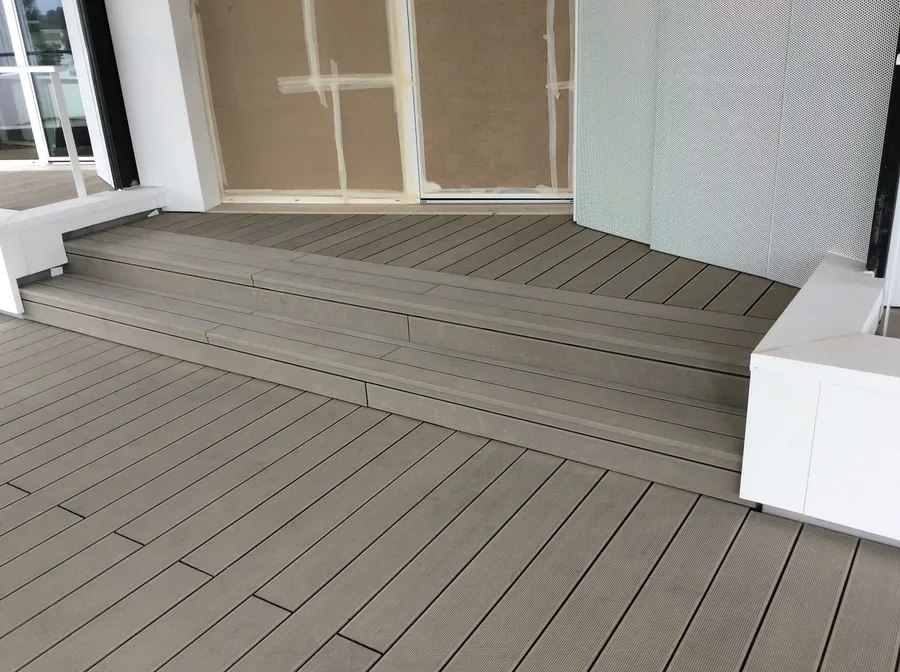Grey composite decking steps connecting two levels of the balcony, beside a façade still under protection.