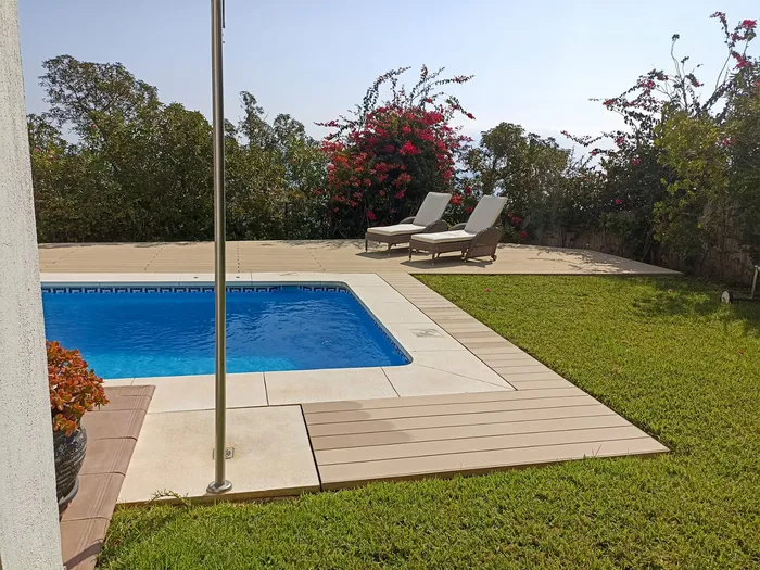 Piscine d'angle bordée de terrasse composite claire et pelouse verdoyante.