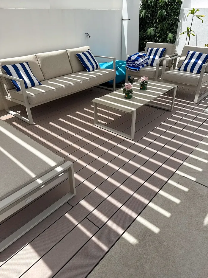 Coin salon extérieur sur la terrasse composite CDECK® Beige Rose, canapé et fauteuils à coussins rayés bleu et blanc, table basse assortie.