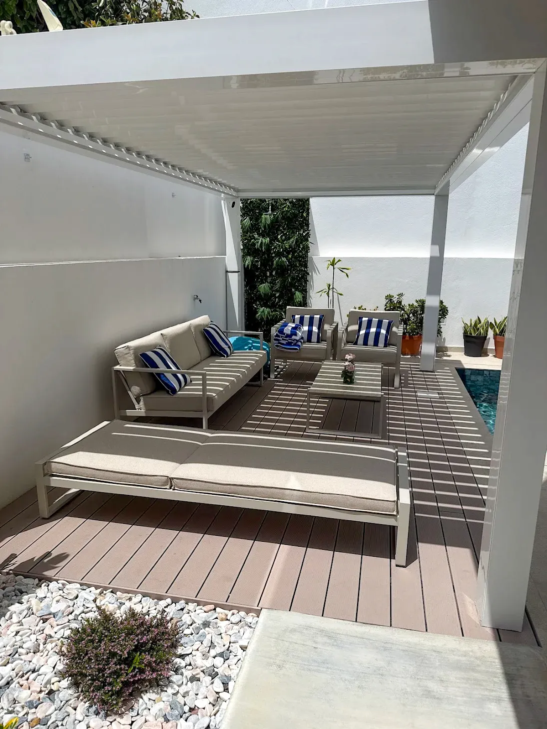 Coin détente sous pergola bioclimatique, terrasse composite CDECK® Beige Rose, salon extérieur et bain de soleil au bord de la piscine.
