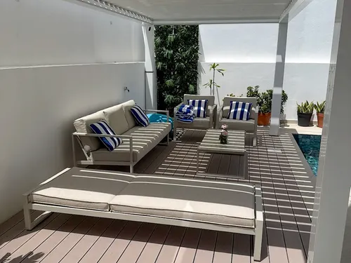 Lounge area under a bioclimatic pergola, CDECK® Rose Beige composite decking, outdoor seating and sun lounger by the pool.