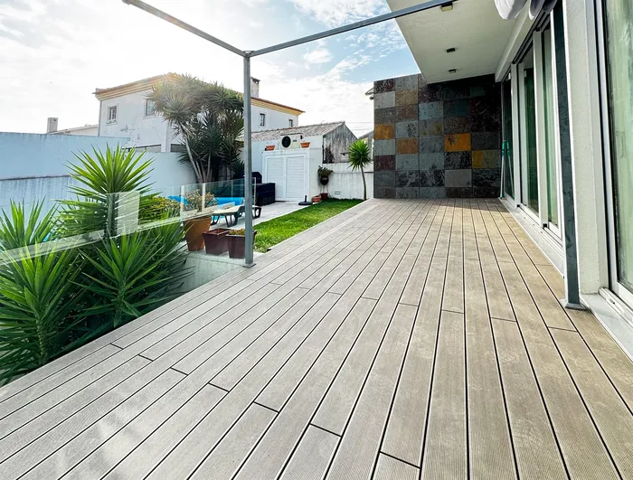Jardin vu depuis la terrasse composite, piscine et transat au soleil, mur en pierre en fond.
