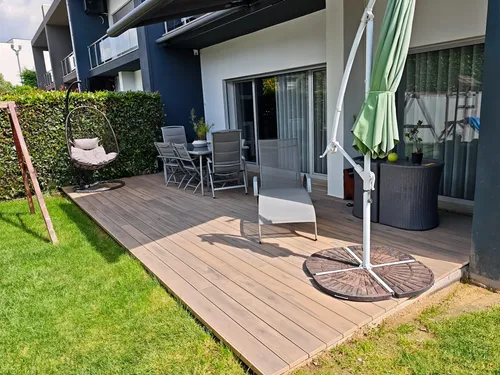 Extended CDECK® Natural Beech composite decking in a rear garden, hanging chair, dining set and sun lounger under a parasol.