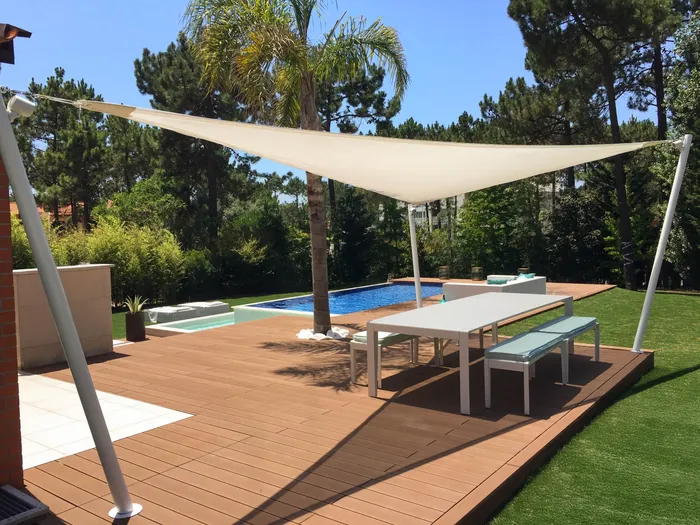Coin repas ombragé par une voile tendue, avec vue sur la piscine et le jardin en arrière-plan.
