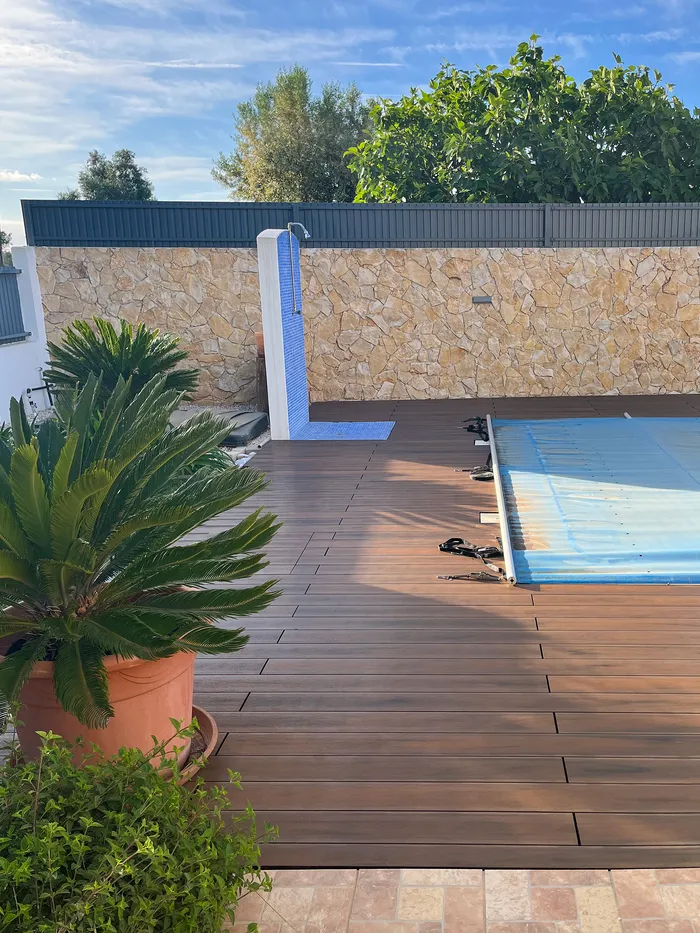 Plante en pot sur la terrasse composite, avec la piscine bâchée et la façade de la maison en fond.