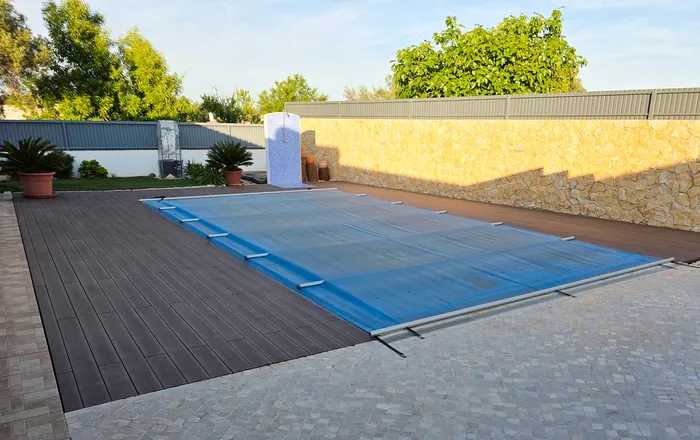 Terrasse composite ensoleillée menant à la piscine, plante en pot et façade jaune de la maison.
