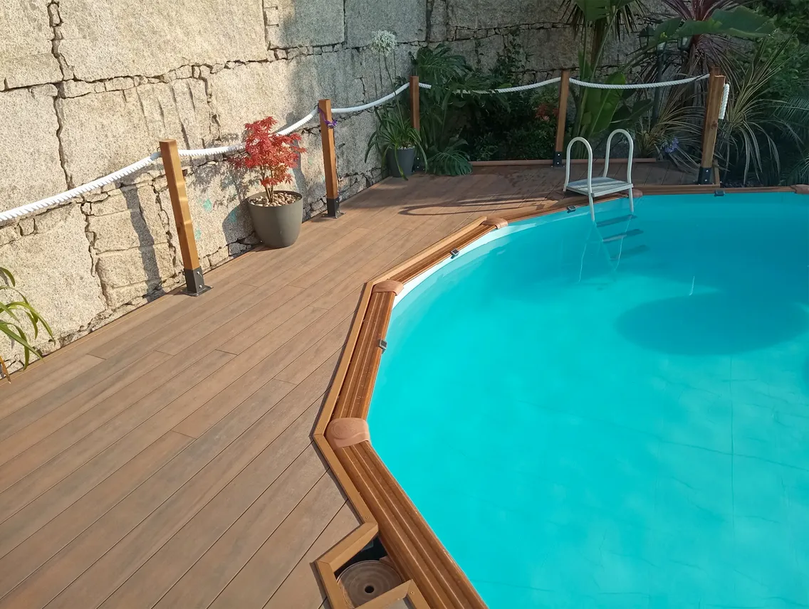 Plateforme en terrasse composite American Walnut qui fait le tour de la piscine hors-sol, poteaux en bois avec corde et plantes tropicales.