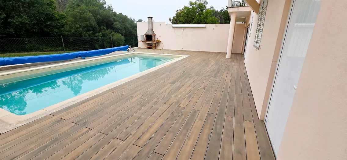 Terrasse composite CDECK® Natural Beech autour de la piscine et le long de la façade de la maison, barbecue contre le mur en arrière-plan.