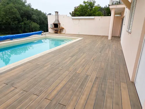 Deck compósito CDECK® Natural Beech à volta da piscina e ao longo da fachada da moradia, churrasqueira junto ao muro ao fundo.