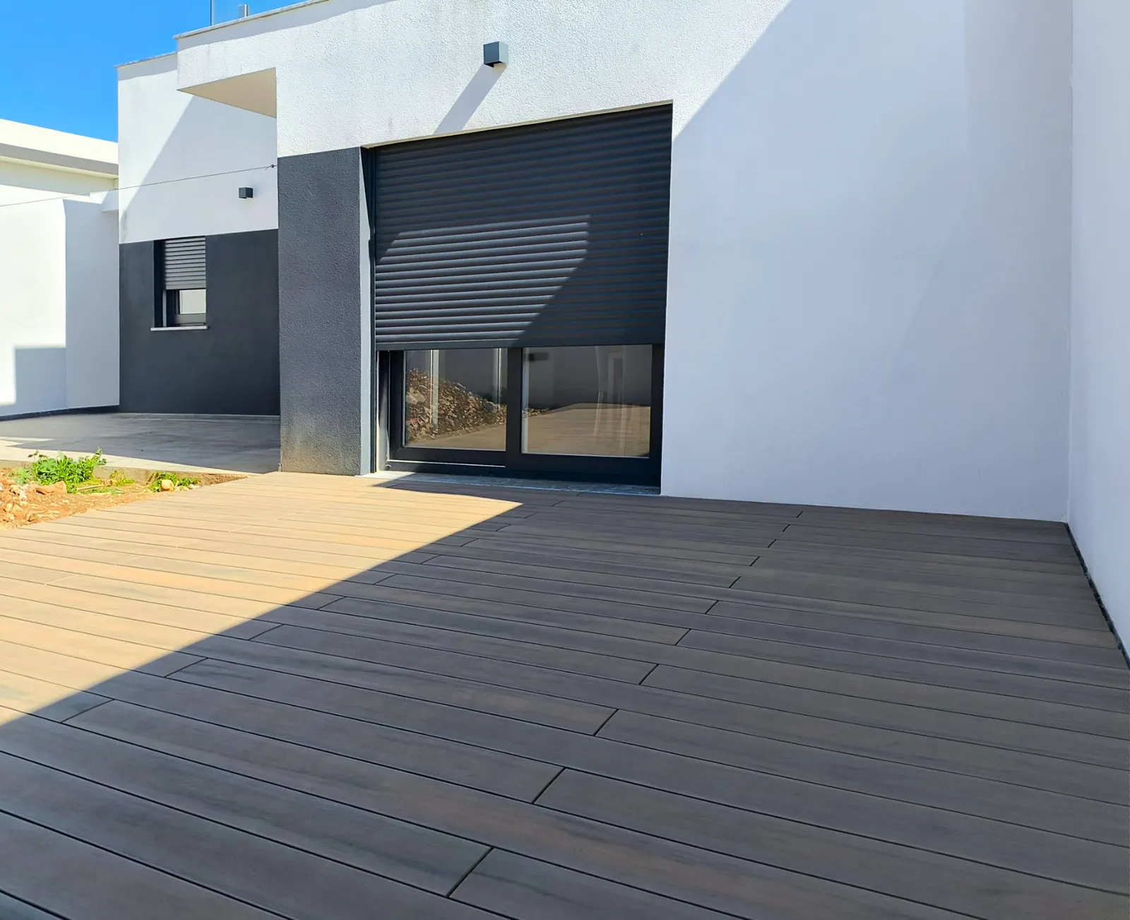 Deck compósito CDECK® Natural Beech nas traseiras de moradia branca e antracite, junto à janela com estore.