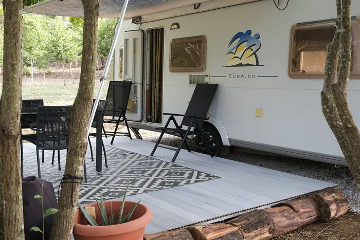 Salon repas sous l'auvent, terrasse ouverte sur un jardin arboré et une maison voisine.