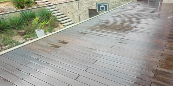 Terrace with CDECK WUUDE® composite decking in American Walnut and a glass balustrade, overlooking a garden