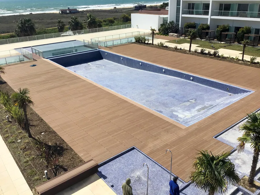 Piscine rectangulaire en finition, terrasse composite en périphérie, plage et océan en fond.