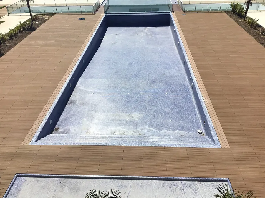 Piscine vue du dessus avec terrasse composite en périphérie et plantations de palmiers.