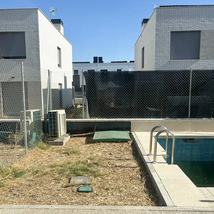 The garden before the work, with wire fencing and shade netting over the low wall, dry grass and the pool alongside.