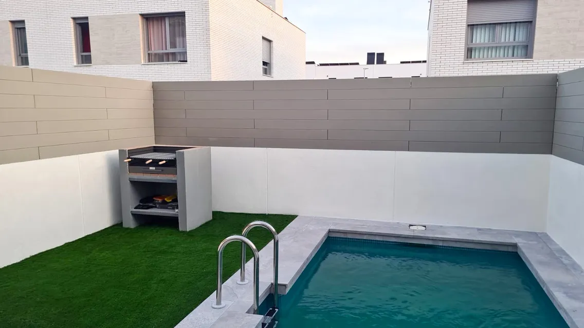 Garden with a swimming pool enclosed by walls clad in CWALL® Grey, with a barbecue and lawn, in Torrejón de Ardoz.