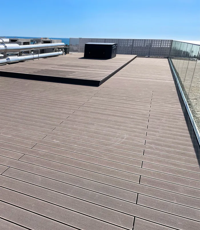 Terrasse composite bordée de galets, avec bac technique et vue lointaine sur la côte.