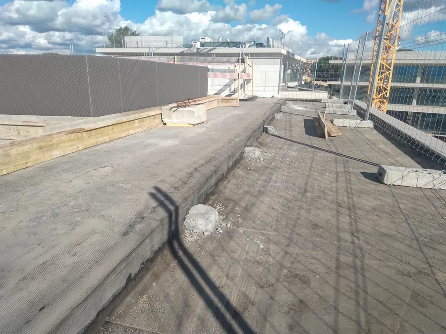 Toiture-terrasse en béton brut avant la pose du revêtement composite, grue de chantier en fond.