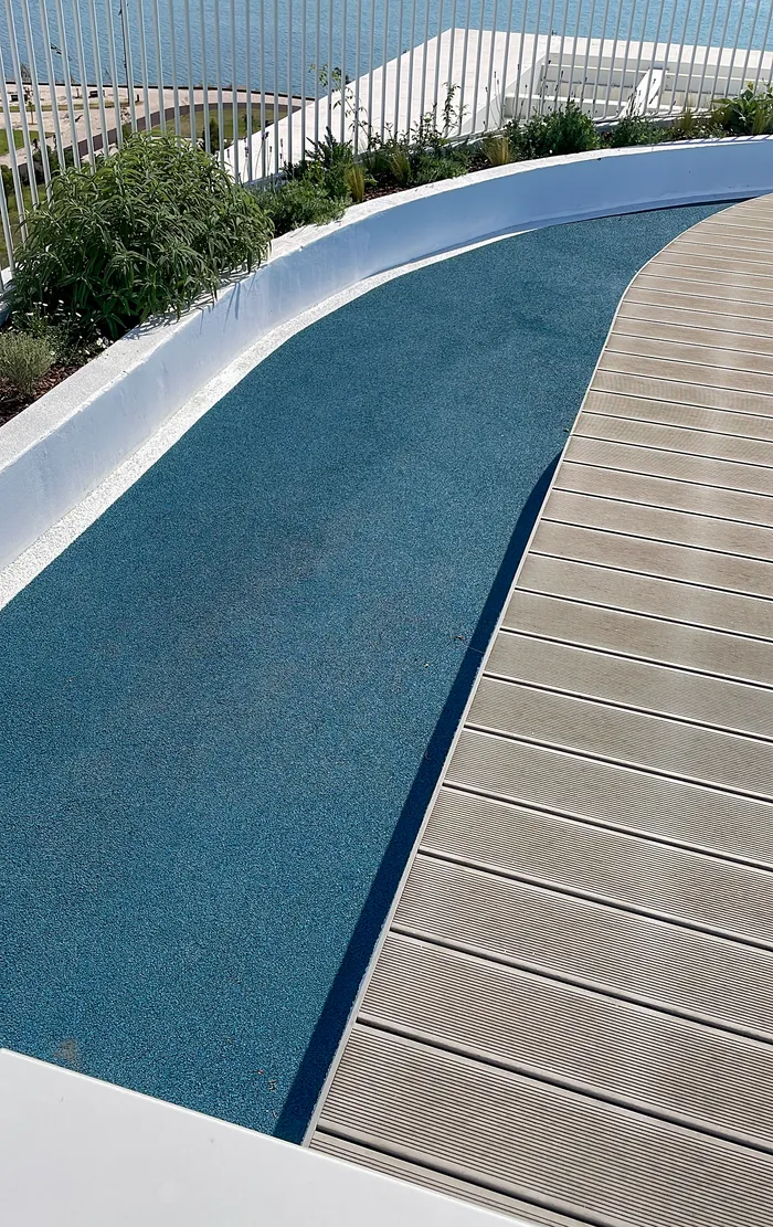 Courbe d'une terrasse composite grise épousant le contour arrondi de la piscine, végétation en bordure.