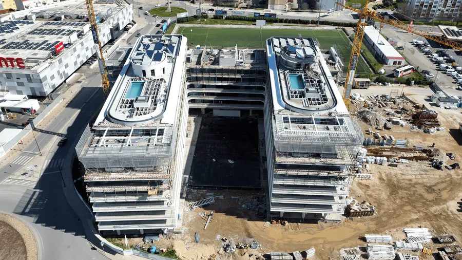 Chantier vu du ciel : structure du bâtiment Nooba en construction, grues et bras de mer en arrière-plan.