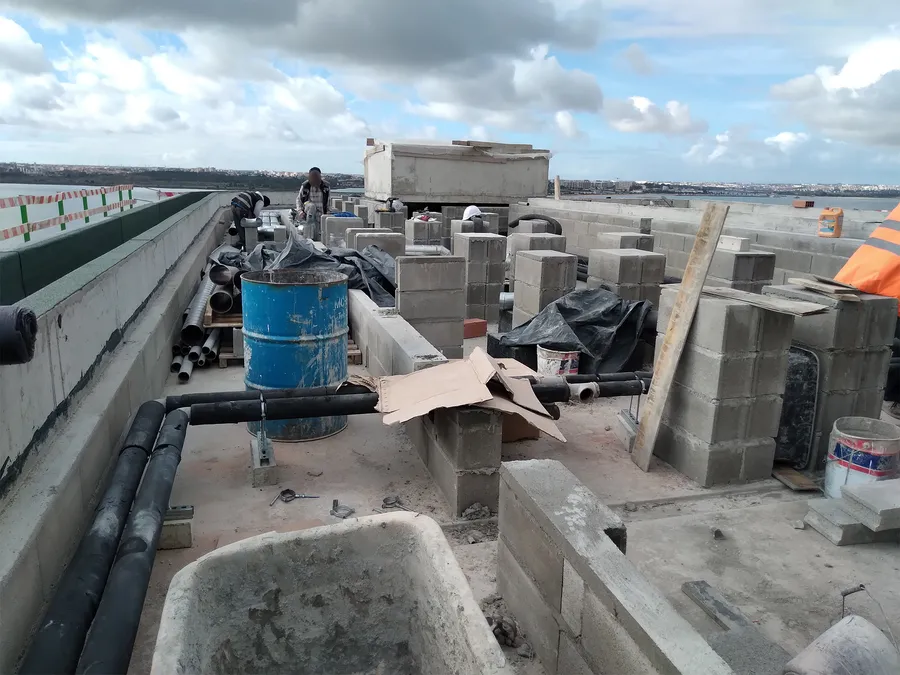 Matériaux et tuyauteries entreposés sur le chantier du toit-terrasse, ouvriers au travail.