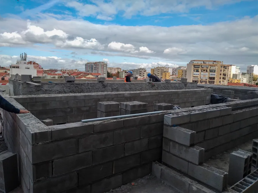 Muret en parpaings en cours de montage sur le toit, immeubles de Barreiro à l'horizon.