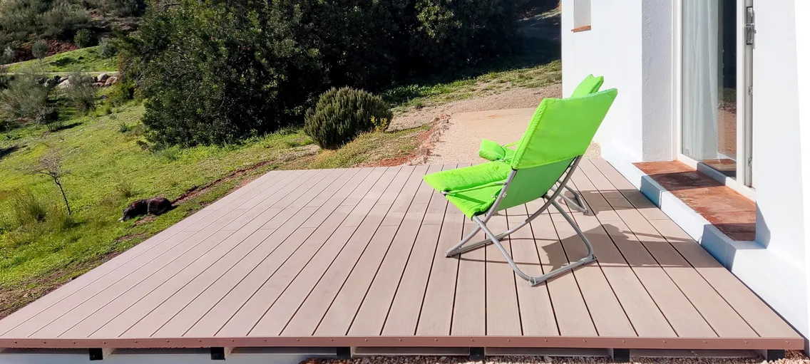 Chaise longue sur la terrasse composite dominant les oliviers, avec un chien allongé dans l'herbe.