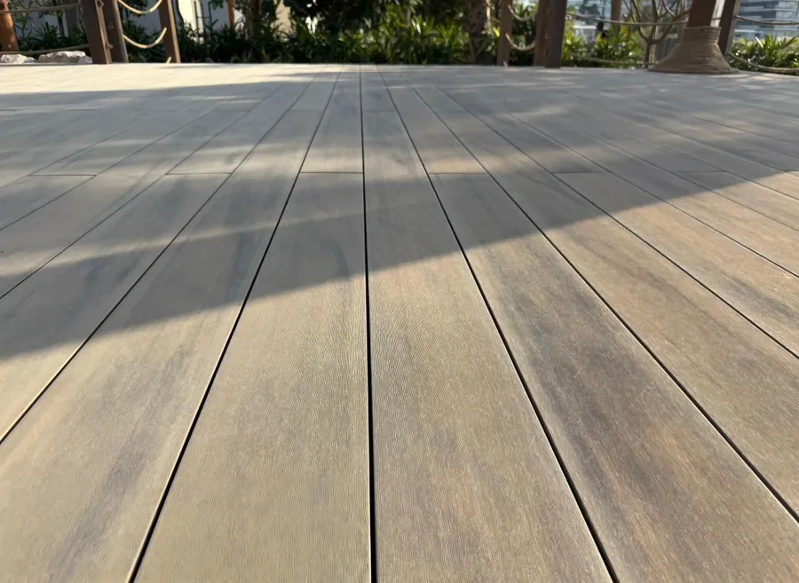 Gros plan sur les lames de terrasse composite imitation bois, ombres de palmiers projetées au sol.